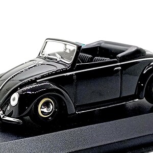 Op de afbeelding: Een zwart schaalmodel van een Volkswagen Kever cabriolet met een glanzende afwerking, chromen bumpers, ronde koplampen en zwarte wielen met zilveren wieldoppen. Het interieur is zwart met zichtbare stoelen op een zwarte ondergrond.