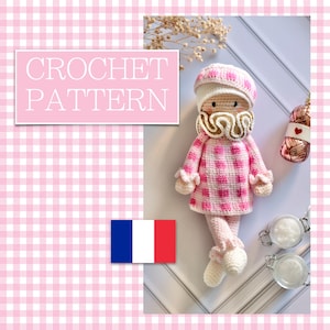 Peut inclure: Une poupée au crochet faite à la main, vêtue d'une tenue à carreaux roses et blancs, d'un chapeau et d'un col à volants. La poupée a un visage crème et est posée sur un fond blanc. Le texte "CROCHET PATTERN" est affiché dans un encadré rose.