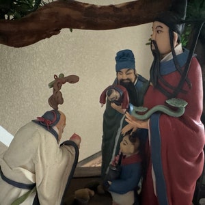 Può includere: Un gruppo di cinque figurine che rappresentano persone in abiti tradizionali cinesi. Le figurine sono in ceramica e sono dipinte con colori vivaci. Le figurine sono disposte in cerchio, con la figurina più grande al centro. Le figurine sorridono tutte e sembrano di buon umore.