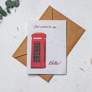 Op de afbeelding: Wenskaart met een illustratie van een rode telefooncel. De tekst "Just wanted to say" en "Hello!" is handgeschreven. De kaart ligt op een bruine envelop.