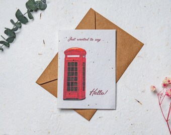 Può includere: Biglietto di auguri con un'illustrazione di una cabina telefonica rossa. Il testo "Just wanted to say" e "Hello!" è scritto a mano. Il biglietto è su una busta marrone.
