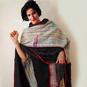 May include: A woman wearing a black dress and a colorful striped shawl with a red border and black pom-poms.