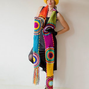 May include: A vibrant, handmade crochet scarf with a matching hat. The scarf features a patchwork design with bright colors like blue, orange, green, and purple, and has colorful fringe. The hat is a fluffy, bright yellow. The scarf is approximately 72 inches long.