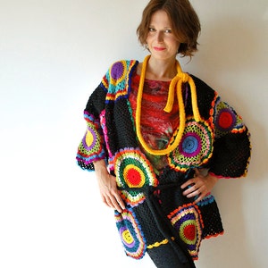 May include: A black crochet cardigan with colorful circular patterns and a yellow crocheted belt. The cardigan has a loose fit and is worn over a colorful patterned shirt.
