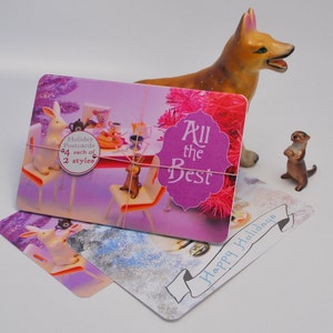 May include: Four pink and purple holiday postcards with a festive table setting, a dog figurine, and an otter figurine. The postcards feature the text "All the Best" and "Happy Holidays".