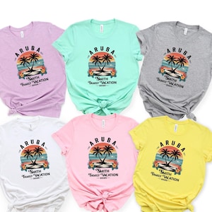 May include: A collection of six short-sleeved t-shirts in various colors, including lavender, mint green, gray, white, pink, and yellow. Each shirt features a graphic with the word "ARUBA", palm trees, and the text "Smith Family Vacation 2025".