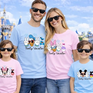 A family of four, consisting of a man, a woman, and two children, posing together in front of a Disney castle. They are all wearing matching t-shirts with Disney characters and the text "Family Vacation".