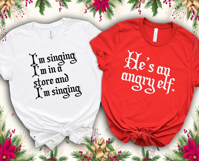 Peut inclure: Deux t-shirts, un blanc et un rouge, avec du texte sur le th&egrave;me des f&ecirc;tes. Le t-shirt blanc porte l'inscription "I'm singing I'm in a store and I'm singing" en script noir. Le t-shirt rouge dit "He's an angry elf" en script blanc. D&eacute;corations de vacances.