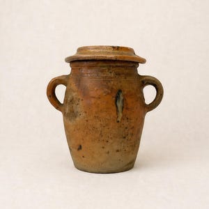 Peut inclure: Un pot en céramique de style antique avec un couvercle. Le pot est de couleur marron terreux et chaleureux, avec deux anses et une surface légèrement texturée. Le couvercle complète l'esthétique vintage. Probablement utilisé pour le stockage.