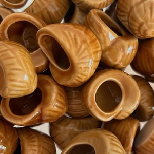 以下が含まれることがあります： 小さな茶色のセラミック製の貝殻型ホルダーのコレクション。各貝殻は滑らかで光沢のある仕上げで、円形の開口部があります。貝殻は集まっており、詳細なリブのテクスチャを示しています。