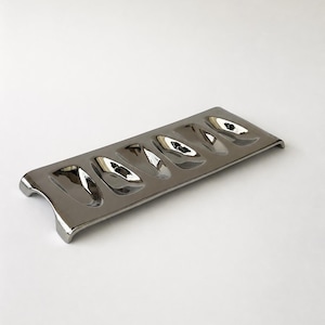 May include: A rectangular, polished silver-toned metal serving tray featuring five distinct, elongated, oval-shaped indentations arranged in a single row. The tray has a smooth, reflective surface and curved edges that elevate the base slightly.