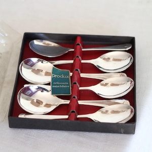 Peut inclure: Un coffret de six cuillères en argent. Les cuillères ont un bord décoratif et sont maintenues en place par des séparateurs rouges dans une boîte noire. L'étiquette indique "Produx orfèvrerie saint hilaire".