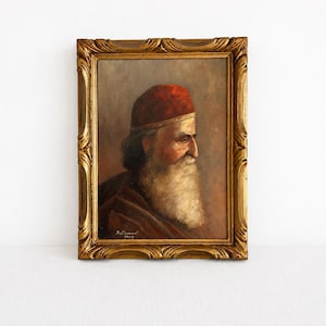 Peut inclure: Une peinture à l'huile dans un cadre doré décoratif représentant le portrait de profil d'une personne âgée avec une longue barbe blanche et un bonnet rouge. L'œuvre est signée Bellonne 1983 en bas à gauche, dans des tons bruns.