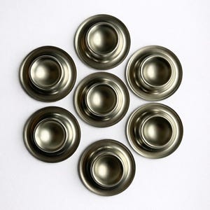 Peut inclure: Sept coquetiers argentés métalliques disposés en cercle sur une surface blanche. Chaque coquetier a une base arrondie et une indentation centrale pour maintenir un œuf. Les coquetiers ont une surface brillante et réfléchissante.