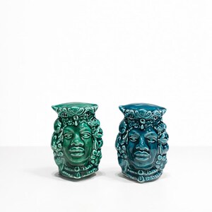 Peut inclure: Deux sculptures de visage en céramique, l'une vert émeraude et l'autre bleu sarcelle. Chaque sculpture présente un visage détaillé avec une coiffe ornée et une base en piédestal. Les sculptures sont probablement des objets décoratifs.