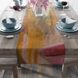 May include: A dining table set for a meal, featuring a colourful abstract art table runner. The table is set with teal-coloured bowls, plates, silverware, and wine glasses. A vase of pink lilies adds a floral touch to the setting.