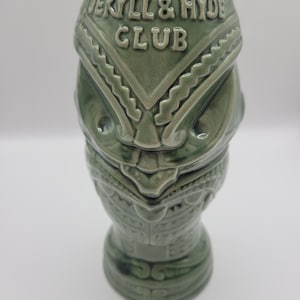 May include: Green ceramic tiki mug with the text "JEKYLL & HYDE CLUB" embossed on the front. The mug has a detailed, stylized design with a tribal or Polynesian theme. The mug is a light green color.