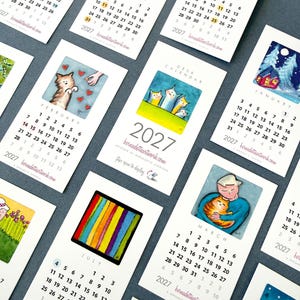 May include: A collection of 2027 desk calendar cards featuring various watercolor illustrations. Each card displays a specific month, numbered dates, and the website bernadetteartwork.com. The artwork includes cats, winter scenes, and colorful patterns.