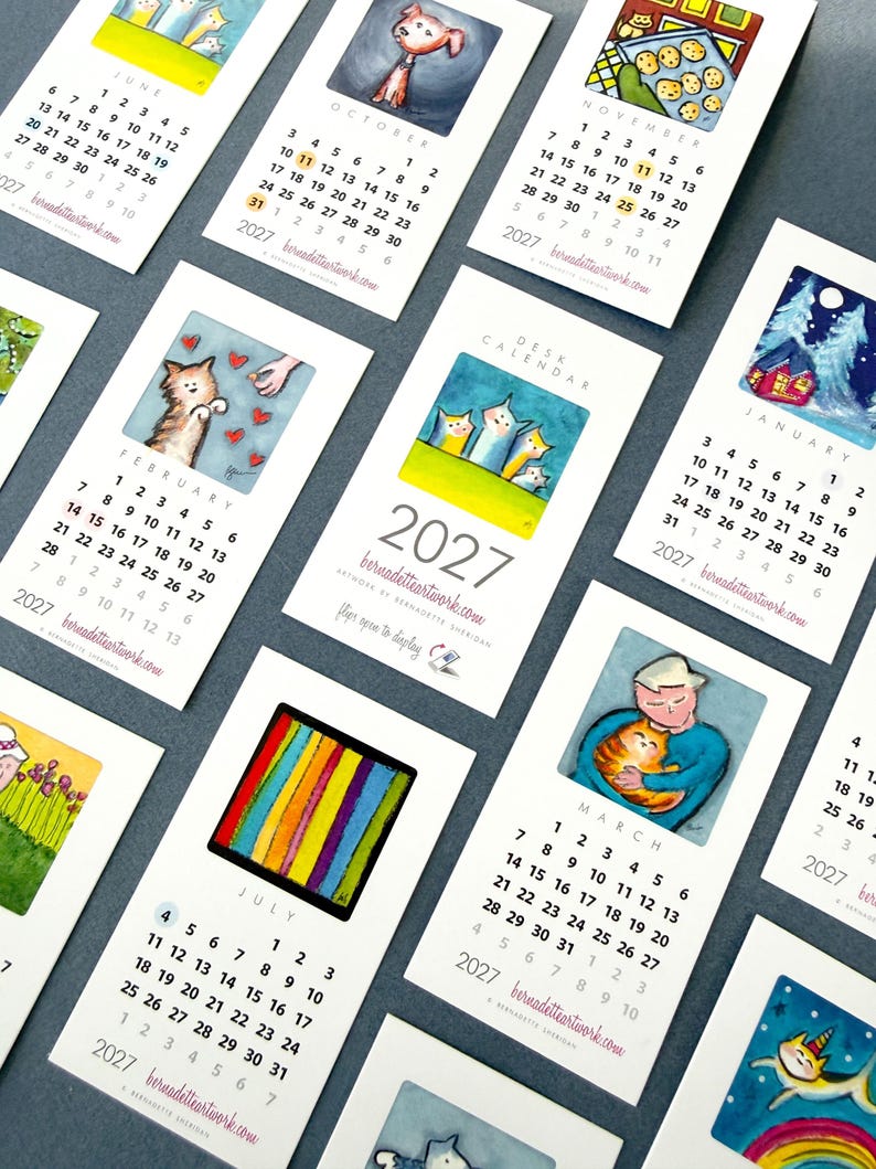 May include: A collection of 2027 desk calendar cards featuring various watercolor illustrations. Each card displays a specific month, numbered dates, and the website bernadetteartwork.com. The artwork includes cats, winter scenes, and colorful patterns.