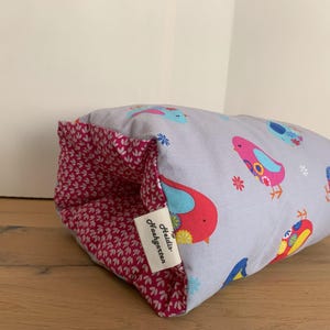 Könnte beinhalten: Ein graues und rosa Kissen mit einem Vogelmuster. Das Kissen hat ein Etikett mit der Aufschrift "Heidi's Kindergarten".