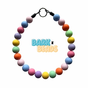 May include: A colourful rainbow beaded necklace with a black clasp and the text "BARK x BEADS".