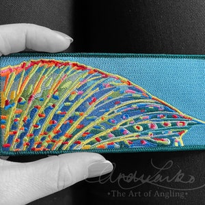 May include: A colorful embroidered patch with a blue, green, yellow, orange, and red design. The patch is shaped like a fish fin and has a green border.