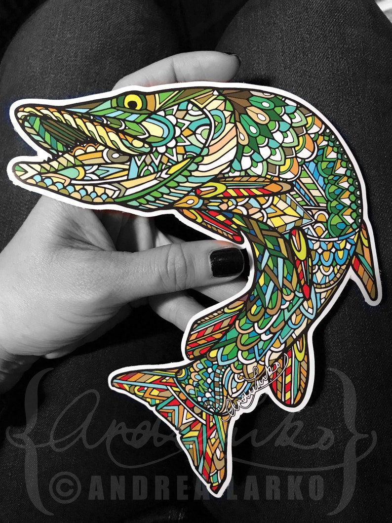 May include: A colorful, intricate, patterned sticker of a fish with a green, blue, yellow, and red design. The sticker is on a hand, and the artist's signature is visible in the lower right corner.