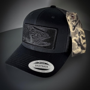 Peut inclure: Casquette de camionneur noire en mesh avec un patch de poisson brodé noir et un autocollant ovale argenté qui indique "The Authentic Yupoong Snapback Yupoong Since 1974".