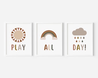 May include: Three framed art prints with a minimalist design. The first features a sun with the word "PLAY", the second a rainbow with "ALL", and the third a cloud with "DAY!". The color palette includes brown, beige, and muted tones.