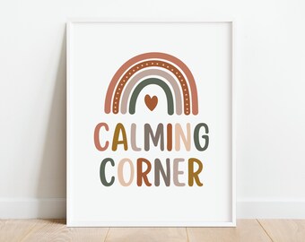 Puede incluir: Una impresión enmarcada en blanco con un arcoíris en tonos marrones, rosas y verdes con un pequeño corazón en el centro. El texto "CALMING CORNER" está debajo del arcoíris en una fuente colorida.