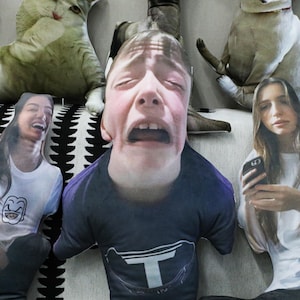 May include: A set of four decorative cushions featuring different faces. The cushions are made of soft fabric and have a realistic look. The faces on the cushions include a person with a surprised expression, a person with a laughing expression, a person with a crying expression, and a person with a neutral expression.
