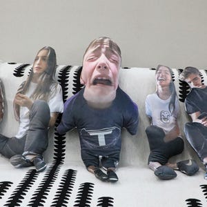 Op de afbeelding: Vijf uitgesneden figuren met overdreven gezichtsuitdrukkingen, gerangschikt op een bank met een zwart-wit patroon. De figuren dragen vrijetijdskleding zoals t-shirts en jeans, die elk een andere emotie uitdrukken.