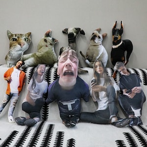 May include: A selection of custom-printed cushions displaying images of pets and people. The cushions feature cats, dogs, and several individuals with diverse facial expressions. The cushions are arranged on a patterned sofa.