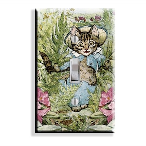 May include: A rectangular light switch cover plate featuring a watercolor illustration of a tabby kitten wearing a blue jacket and a straw hat, surrounded by green foliage and pink flowers. The plate has a central toggle switch and two screws.