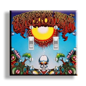 May include: A decorative light switch cover featuring a colorful psychedelic design. The artwork includes a skull, sun, and stylized trees, with the text "Grateful Dead" in a red, ornate font. The cover has two light switches.
