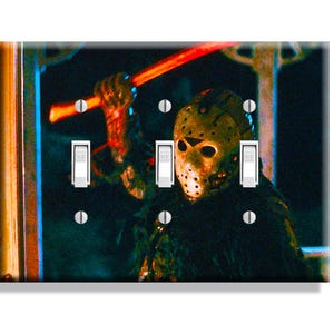 May include: A decorative light switch cover featuring a horror movie scene. The image shows a masked figure holding a red object, with three light switches and six silver screws. The background is dark with blue and green hues.