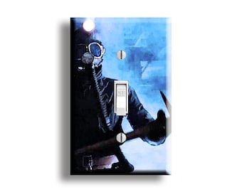 May include: A light switch cover featuring a person in a gas mask and protective gear, set against a blue and white background. The switch is in the "OFF" position. The artwork has a watercolor effect.