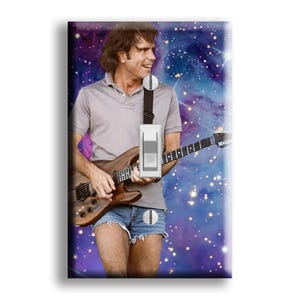 May include: A framed print featuring a man playing a brown electric guitar. He wears a gray polo shirt, denim shorts, and a white device with a black strap. The background is a vibrant galaxy of purple, blue, and white.