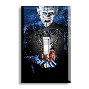 May include: A decorative light switch cover featuring a stylized image of a character with a pale face and pins, holding a small box. The background is dark with blue accents. The switch is white with the word "LIFE" printed on it.