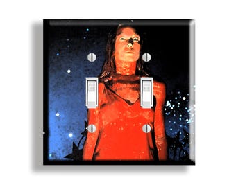 May include: A double light switch wall plate featuring a graphic print of a figure in a red dress against a dark blue starry background. The plate has two white toggle switches and four silver screws, with the word OFF visible on each switch.