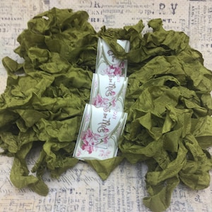 May include: Olive green ruffled ribbon and decorative ribbon spools. The spools have a floral design and the text "Rêves de Nice". The ribbon is bunched together, creating a textured and layered appearance. Ideal for crafting and embellishments.