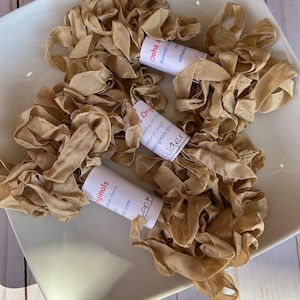 May include: Three spools of beige silk ribbon, each wrapped with a label. The labels read "Oohs & Originals", "Suger", and "Oohs & Originals".