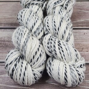 May include: Two skeins of yarn in a white and black speckled pattern. The yarn is soft and fluffy, and would be perfect for knitting or crocheting.