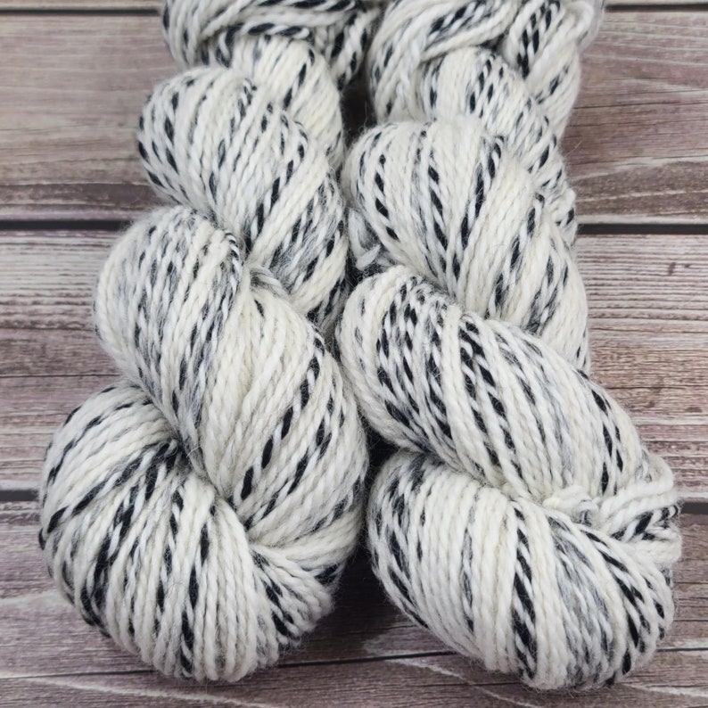 May include: Two skeins of yarn in a white and black speckled pattern. The yarn is soft and fluffy, and would be perfect for knitting or crocheting.