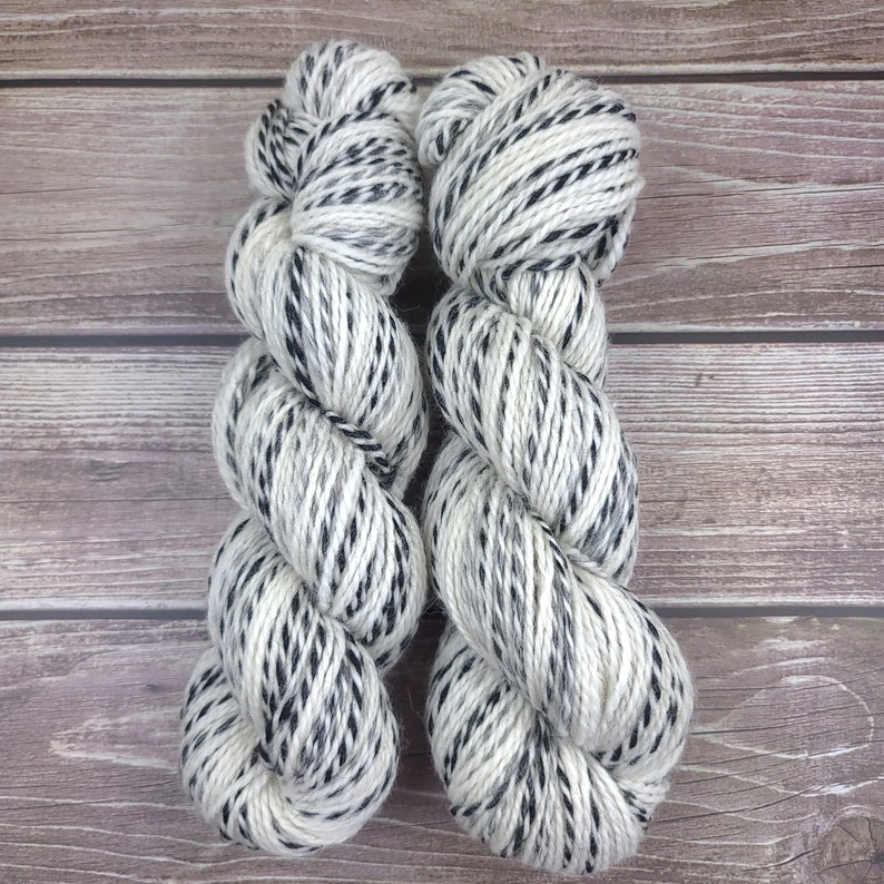 May include: Two skeins of white yarn with black speckles. The yarn is twisted into a spiral shape.