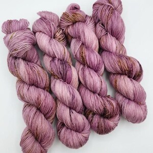 May include: Four skeins of hand-dyed yarn in shades of mauve, plum, and brown. The yarn is twisted into a skein shape, showing the color variations. The yarn is likely for knitting or crocheting projects.
