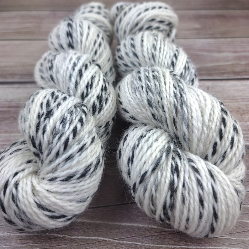 May include: Two skeins of white yarn with black speckles. The yarn is soft and fluffy, and it is perfect for knitting or crocheting.