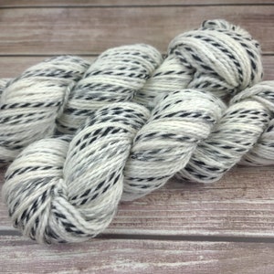May include: A skein of white yarn with black stripes. The yarn is soft and fluffy, and it is perfect for knitting or crocheting.