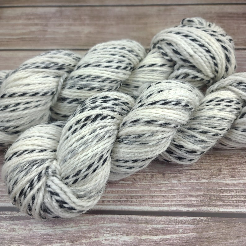May include: A skein of white yarn with black stripes. The yarn is soft and fluffy, and it is perfect for knitting or crocheting.