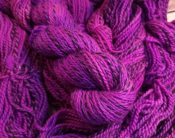 May include: Purple yarn with black flecks, twisted and piled together. The yarn is soft and fluffy, and the colors are vibrant.